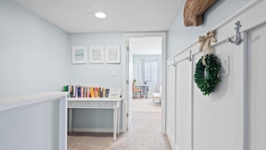 A hallway with a desk, books, a door, and a wreath on the wall. - Santa Rosa Dunes 321 (Pensacola Beach)