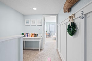 A hallway with a desk, books, a door, and a wreath on the wall. - Santa Rosa Dunes 321 (Pensacola Beach)
