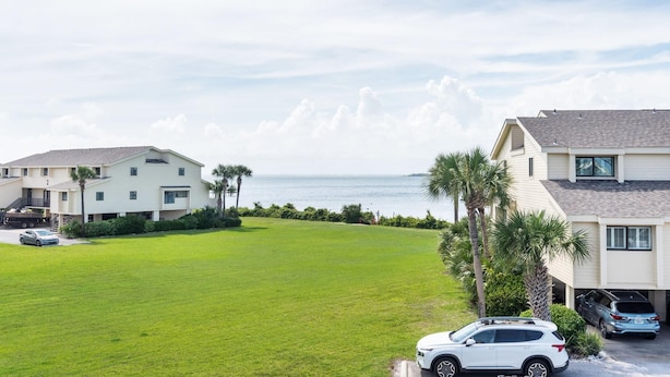 A residential area with a grassy lawn, a white building with a garage, and a view of the ocean. - Santa Rosa Dunes 321 (Pensacola Beach)