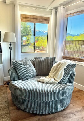 A round, textured sofa with a blanket, positioned in a room with a large window offering a view of a mountainous landscape. - Private Beach Access • Ocean & Mountain Views • Near Olympic National Park (Port Angeles)