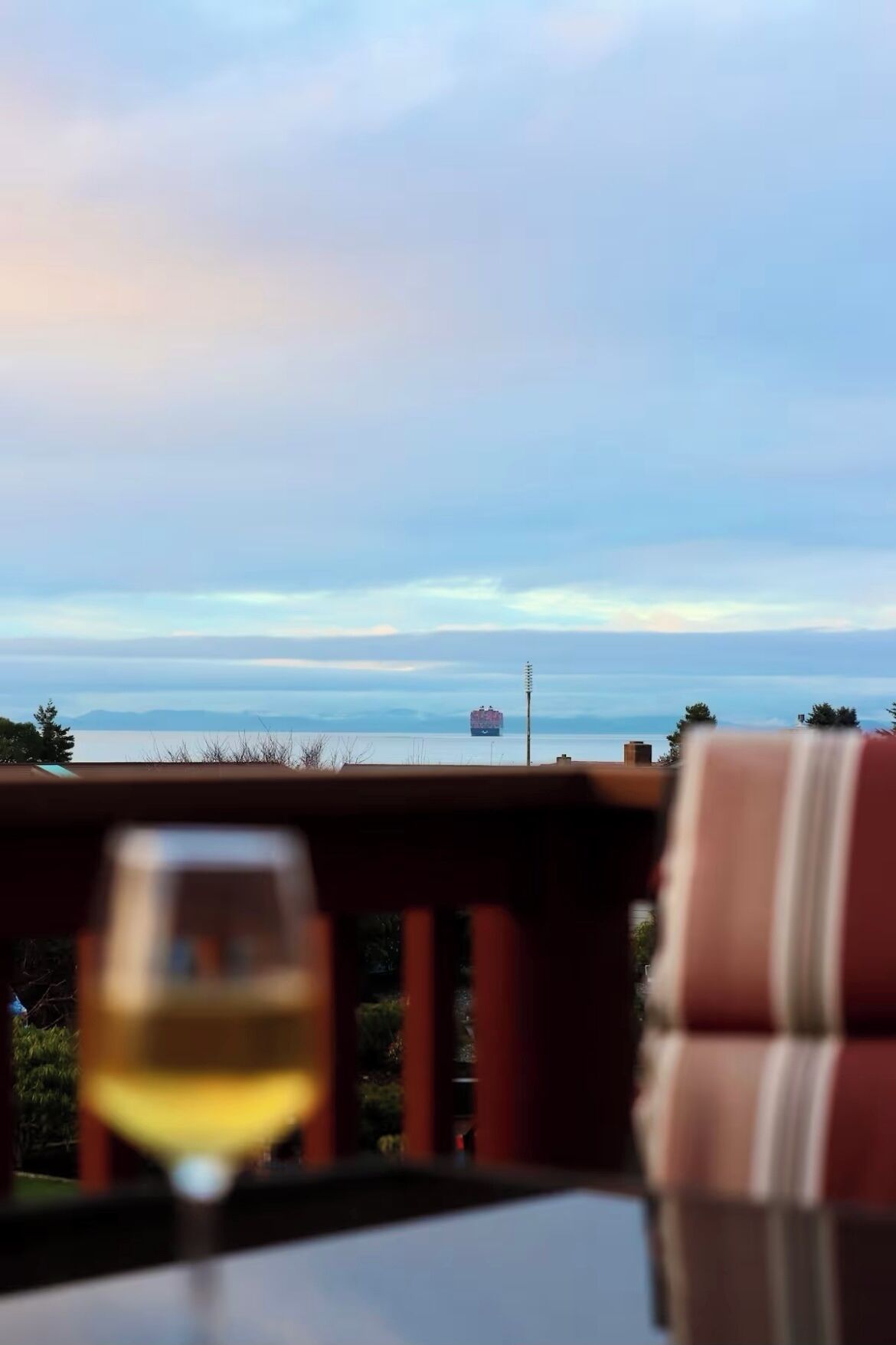 A table with a glass of wine, overlooking a body of water with a ship in the distance.
