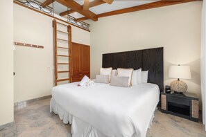 A hotel room with a large bed, a wooden ladder, a dark headboard, a bedside table with a lamp, and a wall-mounted shelf. - Spacious condo in enchanting Playa Flamingo - the most glorious views & 2 pools! (Playa Flamingo)