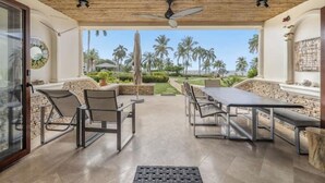 Une terrasse extérieure avec une table et des chaises, un ventilateur de plafond, et une vue sur des palmiers et un ciel dégagé.