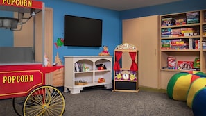 Une salle de jeux avec un chariot à pop-corn, une bibliothèque remplie de jeux de société, un théâtre de marionnettes et une piscine à balles colorée.
