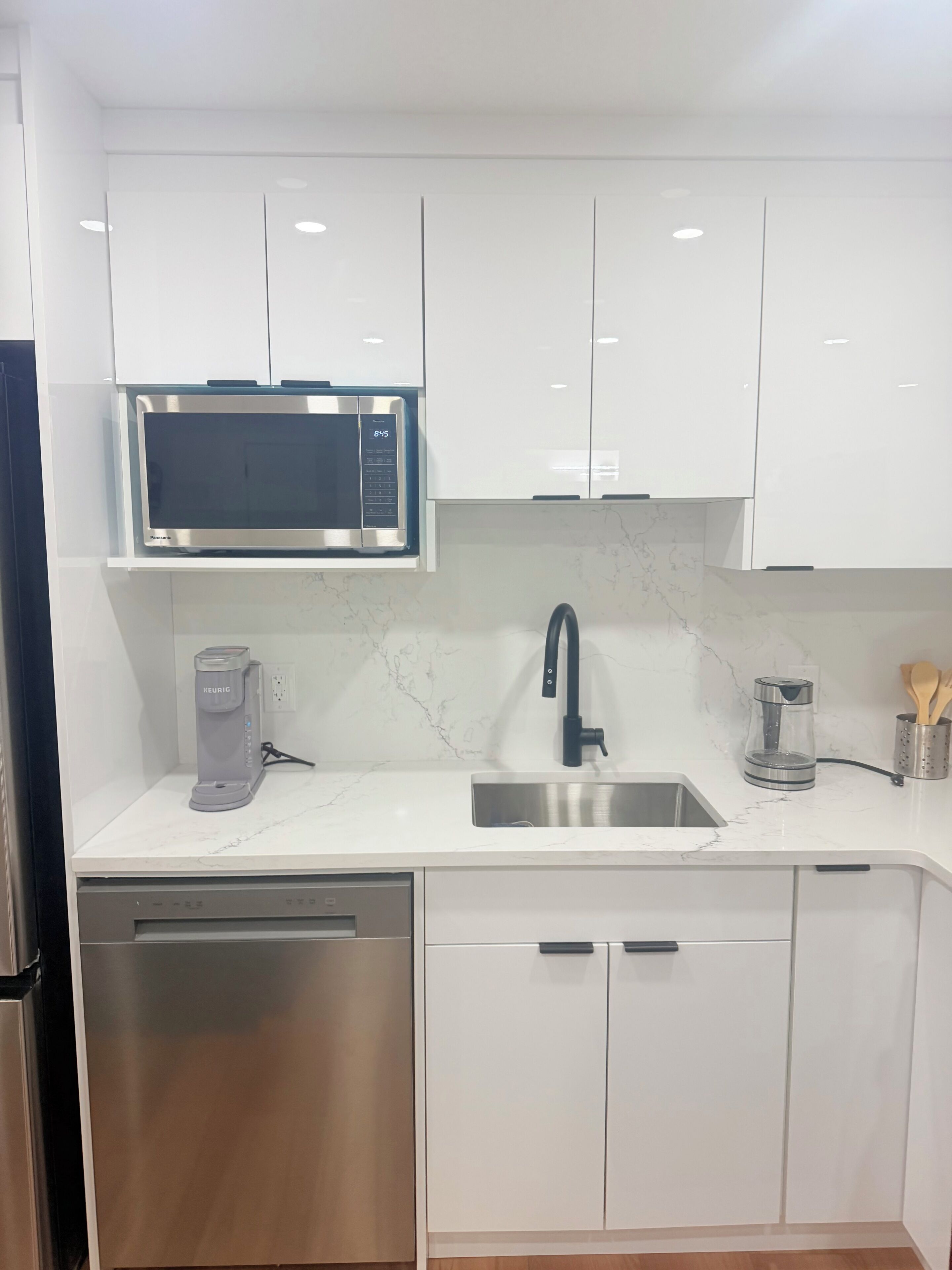 A modern kitchen with white cabinets, a built-in microwave, a coffee maker, and a stainless steel sink.