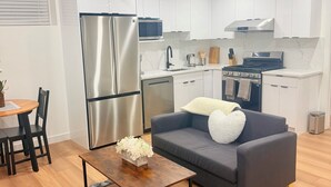Ein modernes Wohnzimmer mit einem grauen Sofa, einem Holztisch und einer Küche mit weißen Schränken und Edelstahlgeräten.