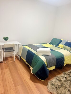 A bedroom with a bed, a small white table, and a potted plant. - Cozy 3 Beds 1 Bath Full Suite (Calgary)