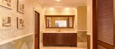 A bathroom with a tiled wall, a wooden vanity with a mirror, and a bench.