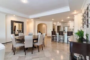 A modern dining area with a round table and chairs, a kitchen in the background, and a decorative mirror on the wall. - Luxury Penthouse in Cap Cana Marina with Jacuzzi (Punta Cana)
