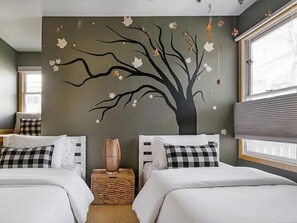 A bedroom with two beds, a wall mural of a tree, a window with blinds, and a bedside table with a vase. - Serene + Spacious Boulder Oasis | Sleeps 10 | 30+ (Boulder)