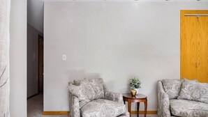 Een kamer met twee gestreepe fauteuils, een klein houten bijzettafeltje met een plant, en een houten deur.
