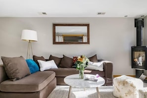 Ein Wohnzimmer mit einer Couch, einem runden Couchtisch, einer Stehlampe, einem Spiegel und einem Kamin.