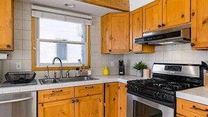 Een keuken met houten kastjes, een roestvrijstalen fornuis, een spoelbak en een raam.