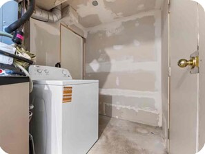 Una lavanderia con lavatrice e asciugatrice, una porta e tubazioni a vista.