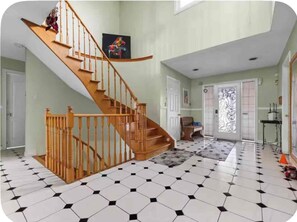 A spacious room with a wooden staircase, a black and white tiled floor, and a large window.