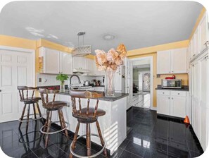 A kitchen with a central island, white cabinets, a black tiled floor, and a vase with flowers on the island. - Stylish Private Room | Free Parking | Fast WiFi | Great Location (Pickering)