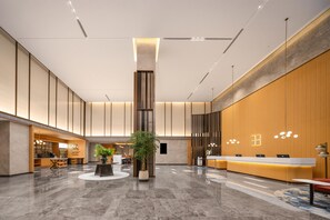 Un vestíbulo amplio con mostrador de recepción, zona de estar y una planta ornamental central.