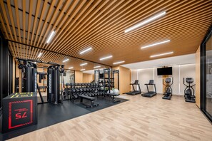 Un gimnasio con varios equipos de ejercicio, techo de madera y suelo negro.