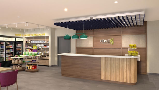 A modern hotel lobby with a reception desk, a snack bar, and a seating area. - Home2 Suites By Hilton Kansas City Speedway (Kansas City)