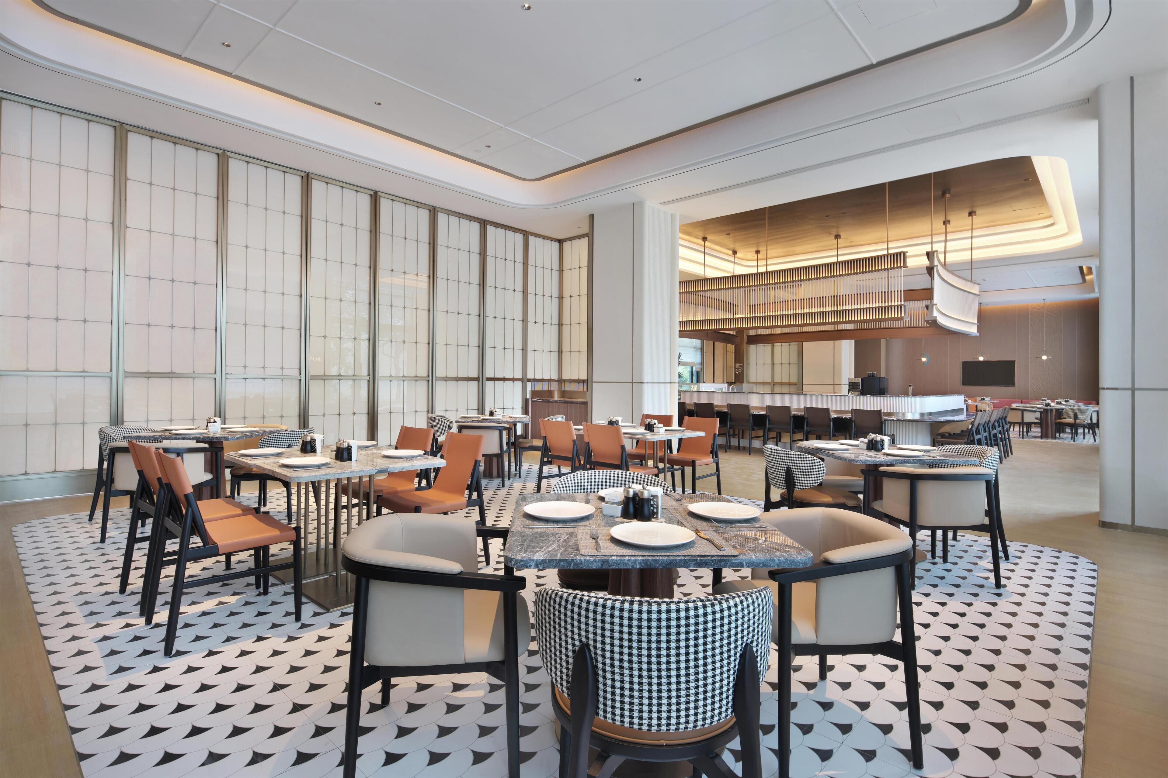 A modern dining area with multiple tables and chairs, a patterned floor, and a large window with a view.