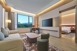A modern hotel room with a sofa, armchair, coffee table, and a TV mounted on the wall. - Hilton Garden Inn Qingdao West Coast Century Avenue (Qingdao)