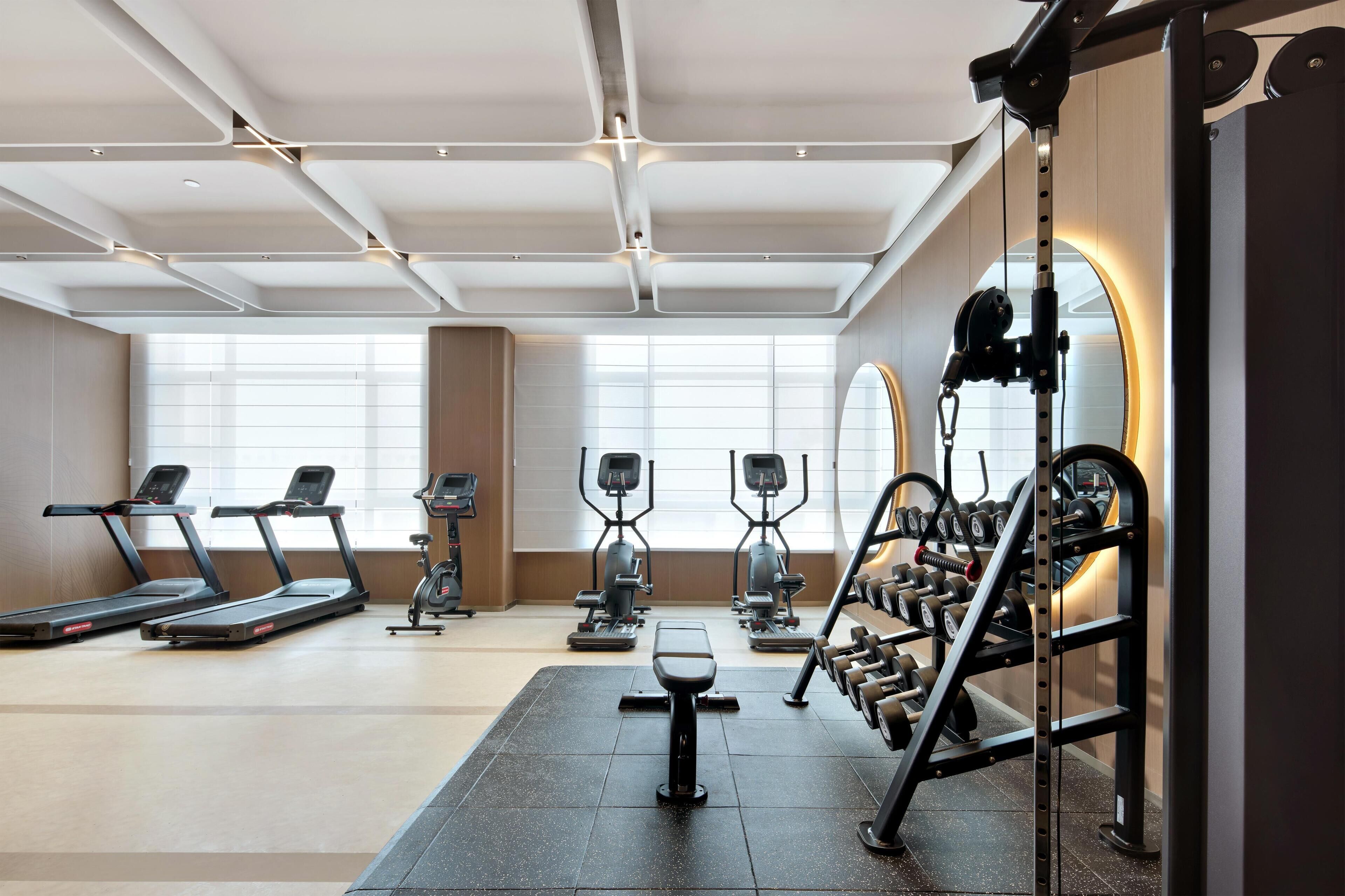 A modern gym with treadmills, elliptical machines, and a weight rack.