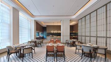 A modern restaurant interior with multiple dining tables and chairs, a patterned floor, and a view into the kitchen area.