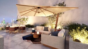 An outdoor seating area with a sofa, chairs, and a table under a large umbrella. - Canopy By Hilton Warsaw (Warsaw)