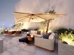 Ein Außenbereich mit einer Sitzecke, inklusive Sofa, Stühlen und Tisch, der von einem großen Sonnenschirm beschattet wird.