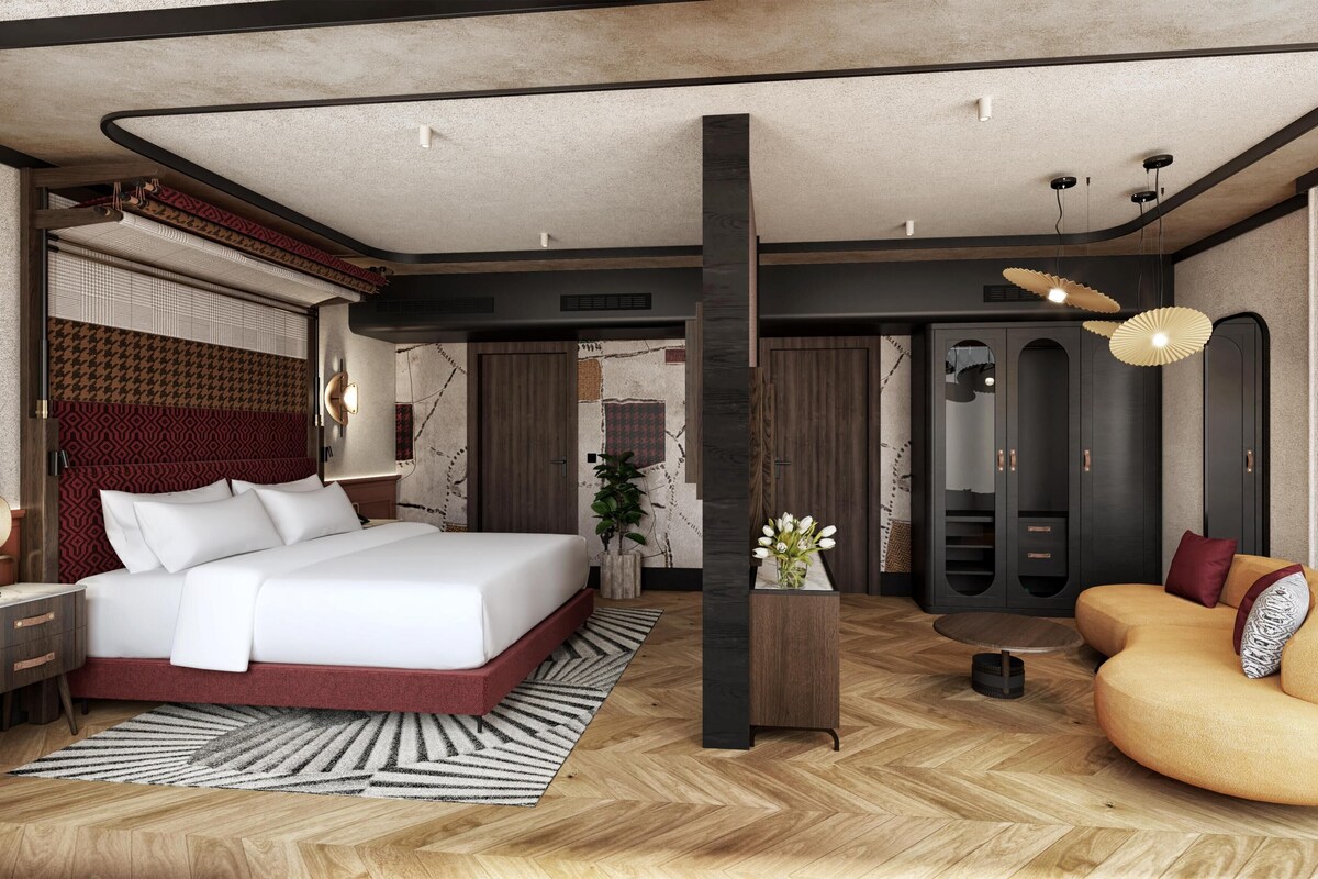 A modern hotel room with a large bed, a sofa, a desk, and a wardrobe.