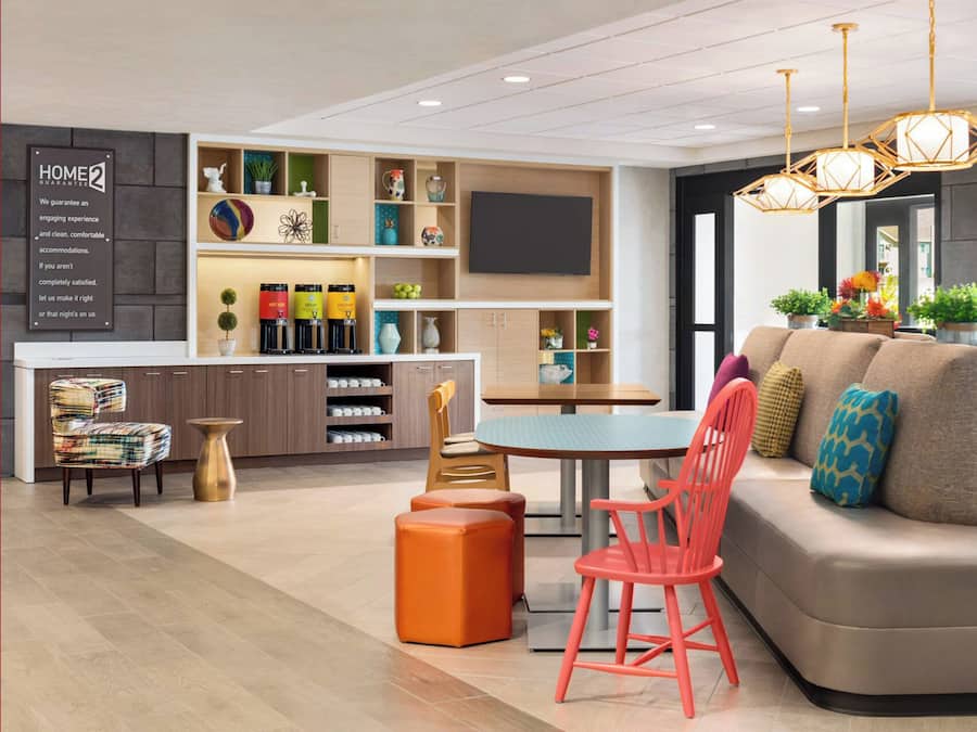 Una habitación de hotel moderna con sofá, sillas, una mesa de comedor, una zona de cocina y un televisor.