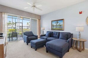 Quarto de hotel com sofá modular, escrivaninha, cadeira, ventilador de teto, pintura e vista para o exterior.