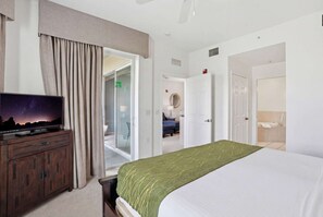 Quarto de hotel com cama, televisão, escrivaninha e banheiro.