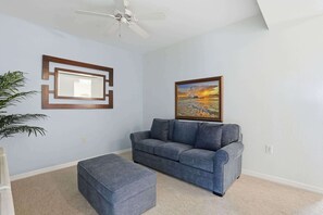 A living room with a gray sofa, a matching ottoman, a ceiling fan, a framed picture, and a potted plant. - 414 - Green Links First Floor -Sleeps 6 (Naples)