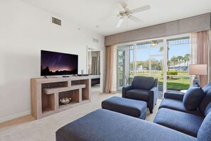 A modern living room with a flat-screen TV, a ceiling fan, and a large window offering a view of the outdoors. - 414 - Green Links First Floor -Sleeps 6 (Naples)