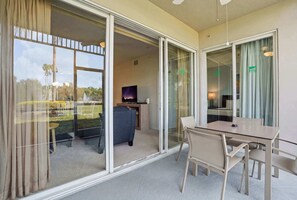 Quarto de hotel com varanda, uma secretária com computador, uma cadeira e uma mesa.