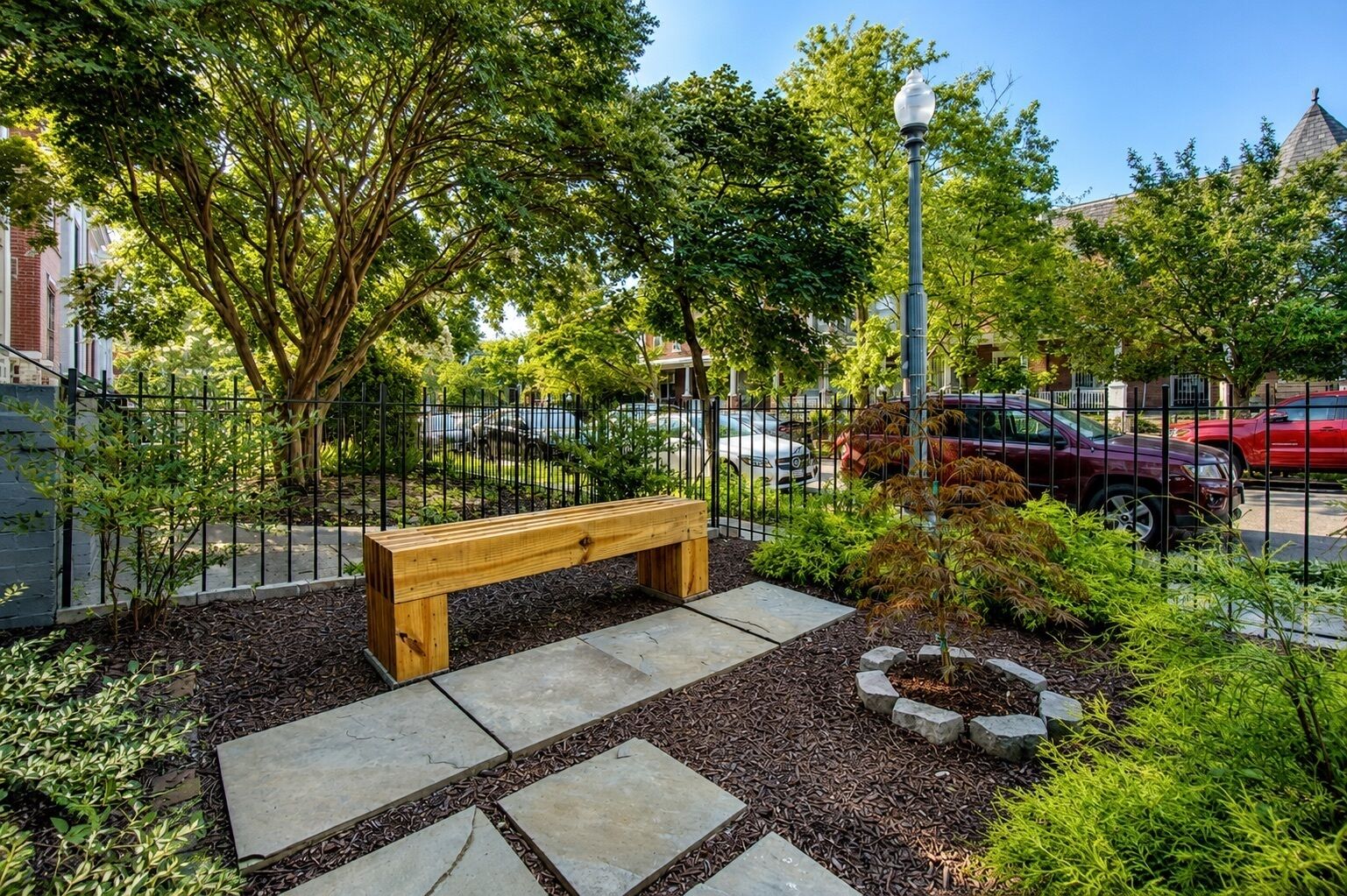 A park with a wooden bench, stone pathways, and a metal fence.