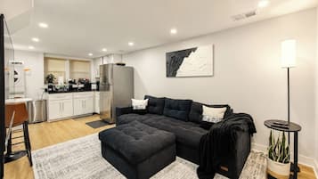 A modern living room with a sectional sofa, a coffee bar, and a kitchen in the background.