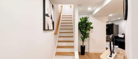 Un interior moderno con una escalera, una planta en maceta, una escultura negra y un televisor de pantalla plana.