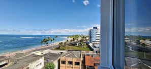 A coastal cityscape with a beach, palm trees, and a mix of modern and older buildings. - COPIA0108 - Edifício Essencial Piata (Salvador)