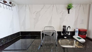 Una cocina compacta con encimera negra, pileta de acero inoxidable, cafetera y una planta pequeña.