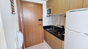 Una cocina compacta con un refrigerador blanco, armarios de madera, un microondas y un lavamanos con grifo.