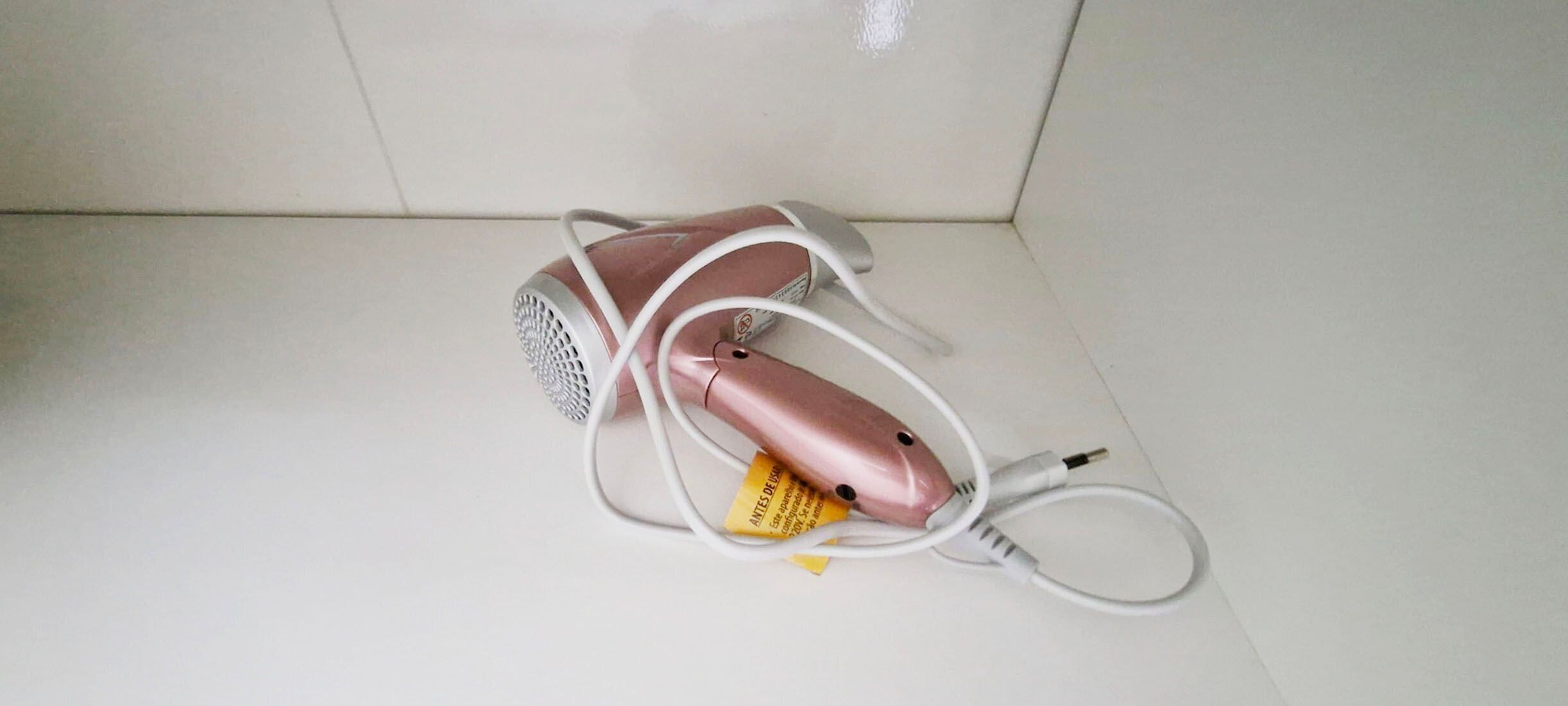 A pink hairdryer with a power cord and a yellow tag on a white tiled floor.