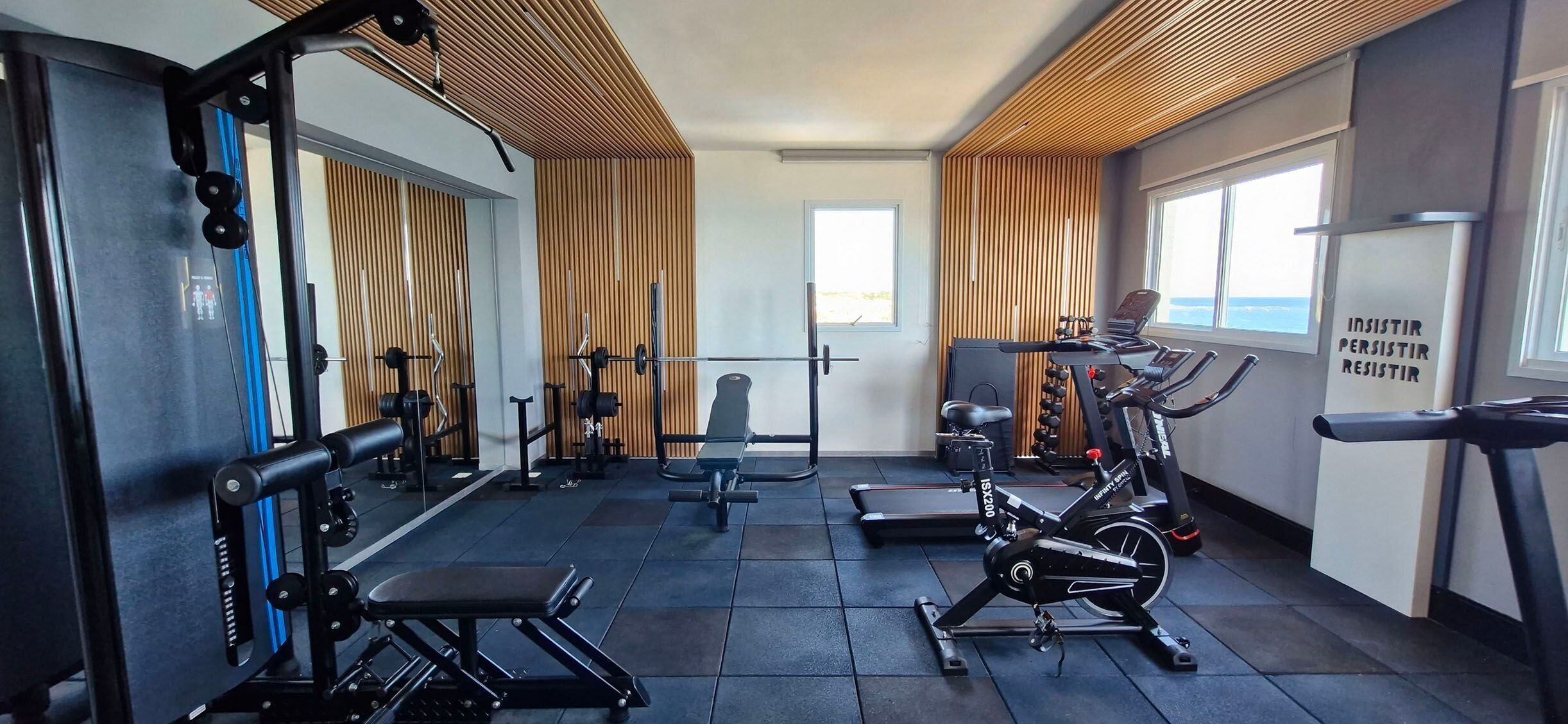 Ein Fitnessraum mit Trainingsgeräten, einer Bank und einer Wand mit motivierenden Sprüchen.