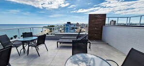 Ein Balkon mit Glastisch, Stühlen und Blick auf Strand und Stadtpanorama.