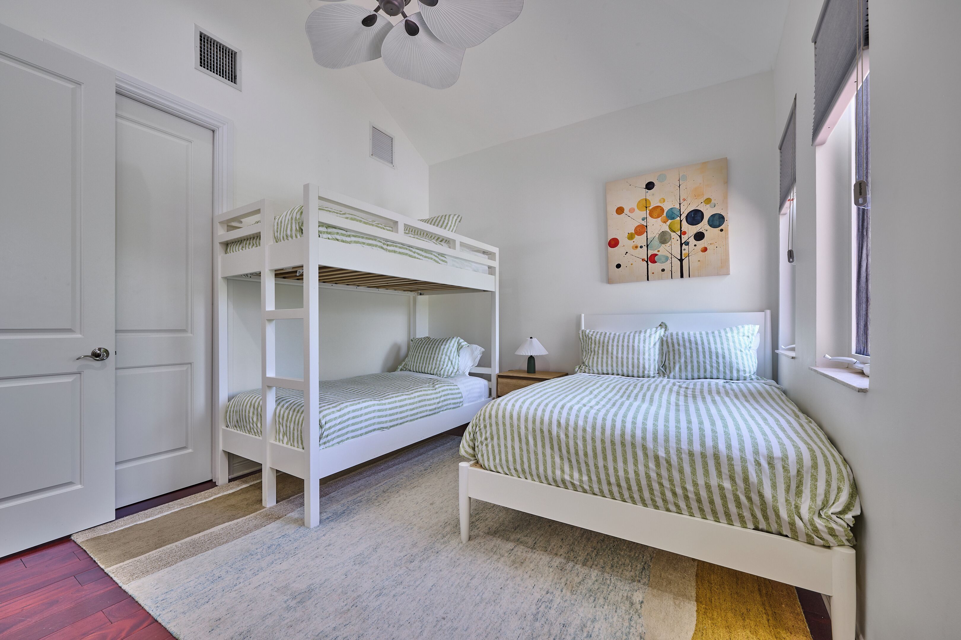 A bedroom with bunk beds, a bedside table, a lamp, a painting, and a window.