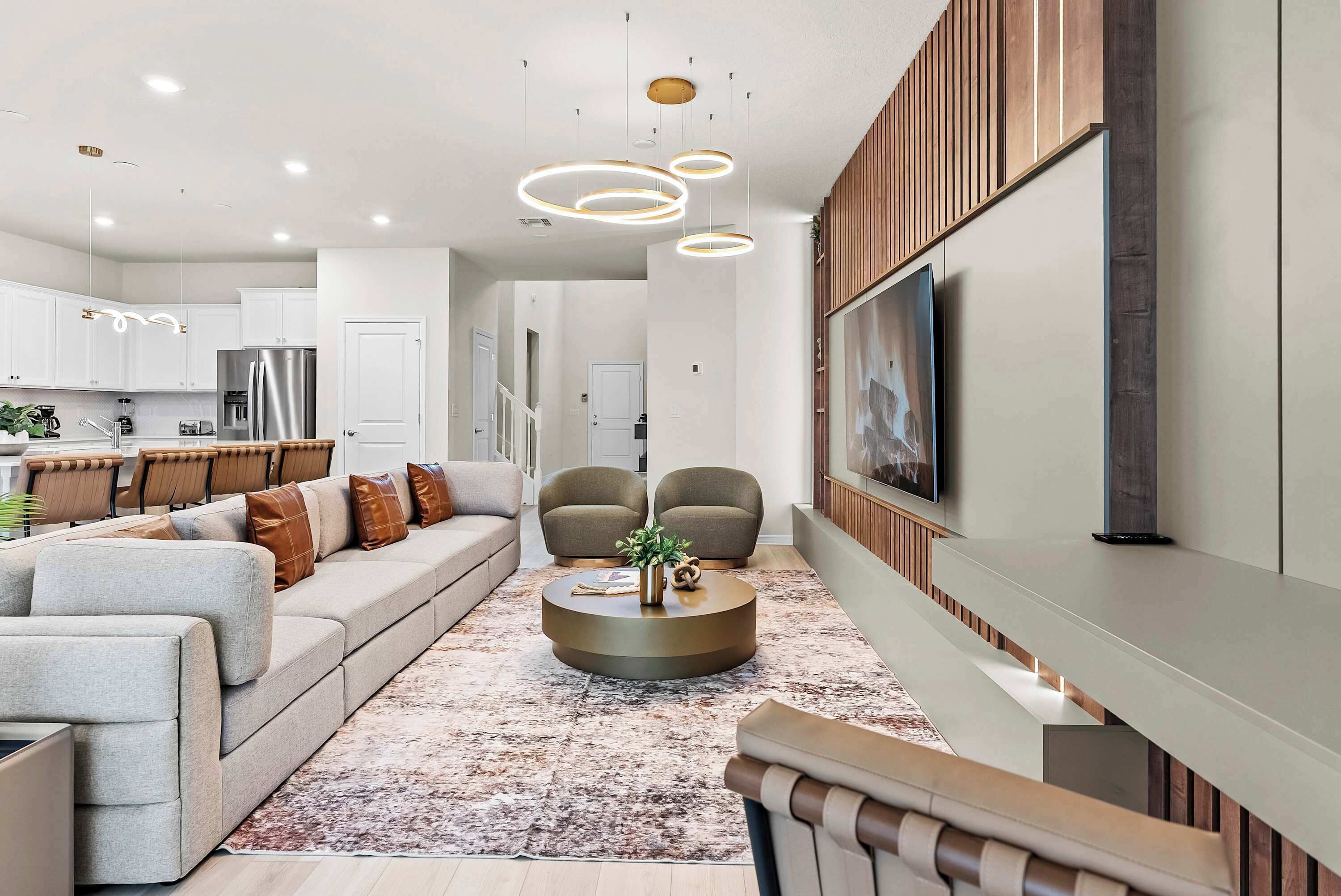 Un salon moderne avec un canapé, des fauteuils, une table basse et un téléviseur fixé au mur.