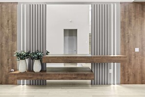 Ein Empfangsschalter mit Holzoptik, flankiert von vertikalen Wandfeldern, und zwei Zimmerpflanzen auf der linken Seite.