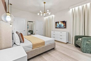 A modern bedroom with a bed, a dresser, a green armchair, and a fireplace image on the wall. - Luxury 8BR Themed Villa With Private Pool (Clermont)