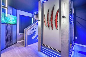 A modern interior with a blue-lit hallway, a dinosaur-themed wall, and a television displaying a natural scene. - Luxury 8BR Themed Villa With Private Pool (Clermont)